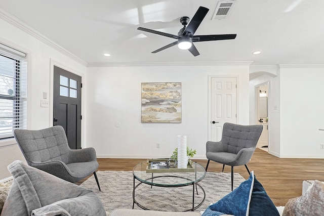 living room featuring visible vents, ornamental molding, arched walkways, baseboards, and light wood-style flooring