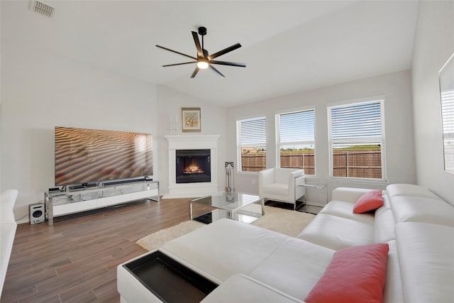 living area with visible vents, a warm lit fireplace, a ceiling fan, wood finished floors, and lofted ceiling