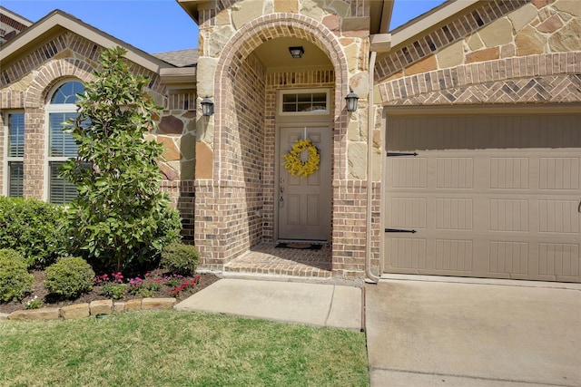 view of exterior entry with a garage, brick siding, and driveway