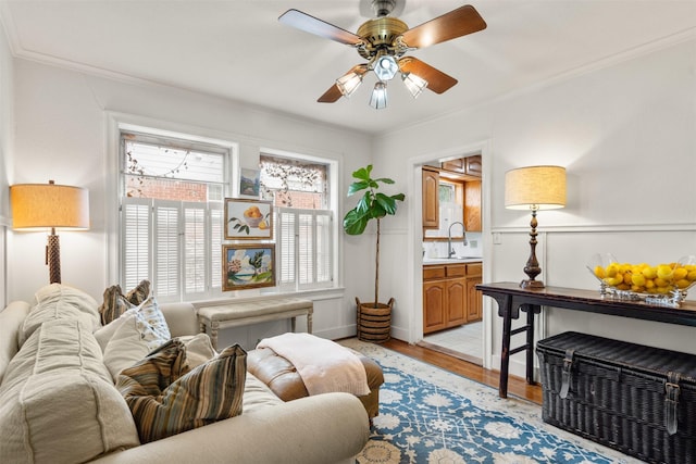 living room with light wood-style flooring, crown molding, ceiling fan, and baseboards