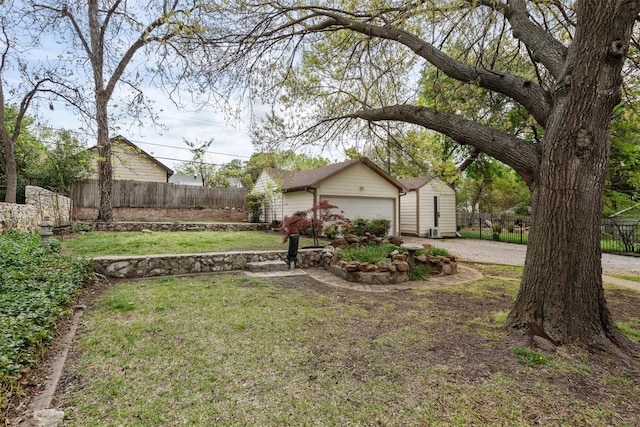 view of yard featuring an attached garage, driveway, fence, and an outdoor structure