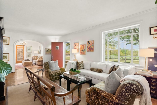 living area with arched walkways, wood finished floors, an inviting chandelier, and ornamental molding