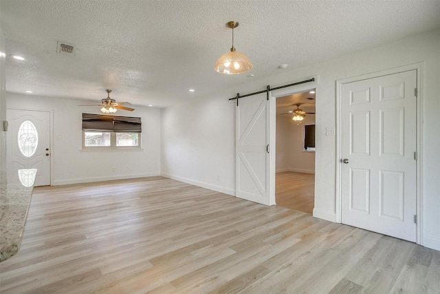 436 Nathan St, Burleson, TX 76028 - unfurnished living room with a barn door, light wood-type flooring, a textured ceiling, ceiling fan, and baseboards