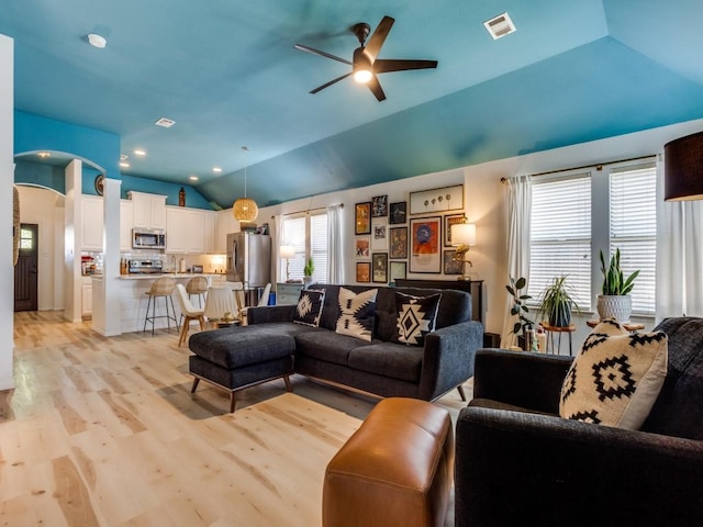 living area with lofted ceiling, light wood-style flooring, visible vents, ceiling fan, and arched walkways