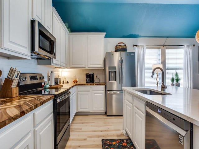 kitchen featuring white cabinets, a sink, light wood finished floors, stainless steel appliances, and decorative backsplash