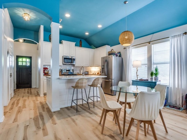 kitchen with white cabinetry, lofted ceiling, hanging light fixtures, stainless steel appliances, and decorative backsplash