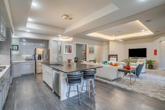 kitchen featuring a breakfast bar, open floor plan, a raised ceiling, stainless steel appliances, and a sink