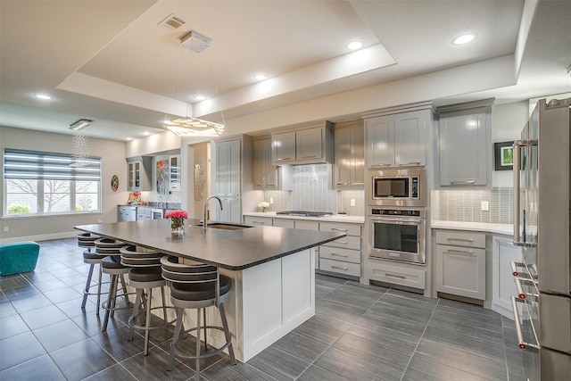 kitchen featuring visible vents, a sink, appliances with stainless steel finishes, a tray ceiling, and dark tile patterned flooring