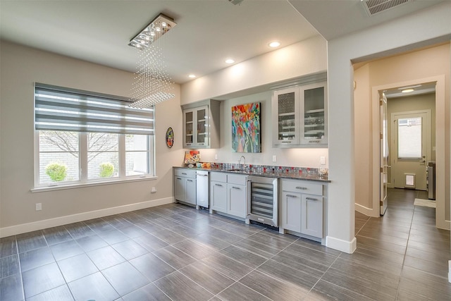 bar with indoor wet bar, baseboards, visible vents, beverage cooler, and a sink