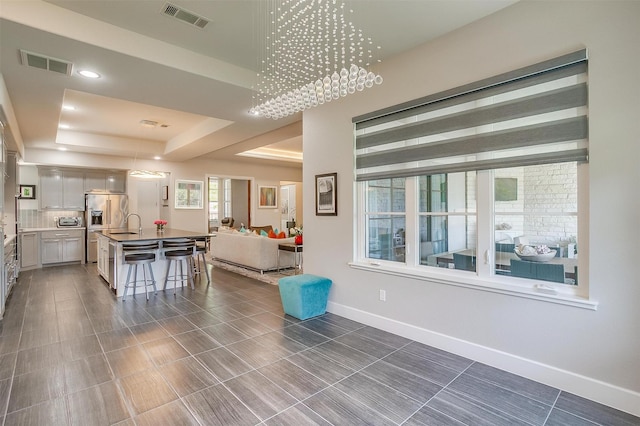 living area featuring a toaster, visible vents, a tray ceiling, and baseboards