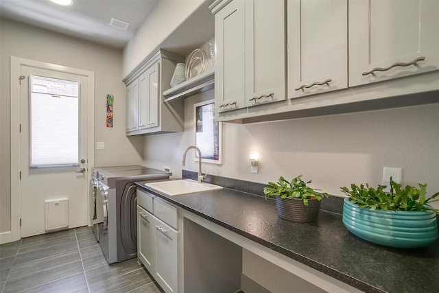 clothes washing area with cabinet space, visible vents, washing machine and clothes dryer, and a sink