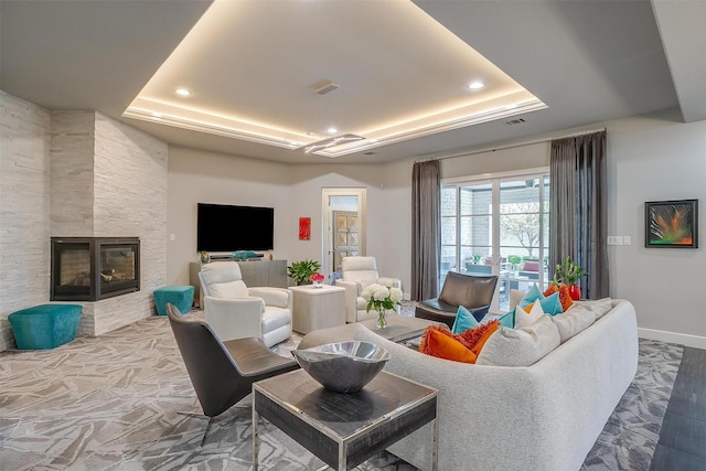 living area with recessed lighting, a multi sided fireplace, a tray ceiling, and baseboards