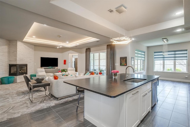 kitchen featuring white cabinets, a sink, dark countertops, a raised ceiling, and open floor plan