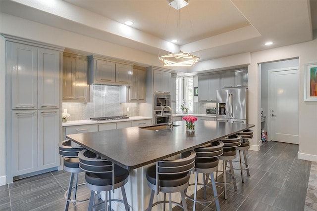 kitchen featuring a sink, a center island with sink, backsplash, a breakfast bar area, and stainless steel appliances