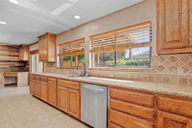 kitchen featuring stainless steel dishwasher, a sink, decorative backsplash, light tile patterned floors, and light stone countertops