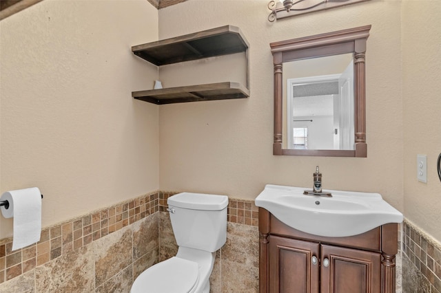 half bath with toilet, vanity, a wainscoted wall, and tile walls