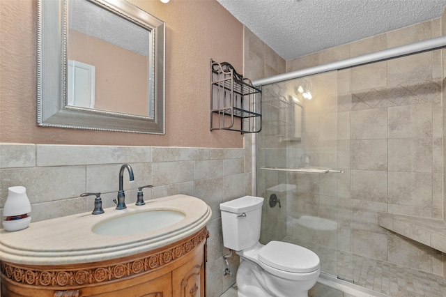 bathroom featuring a textured ceiling, toilet, tile walls, a stall shower, and vanity