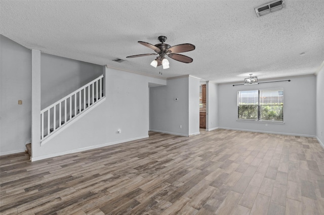 unfurnished living room featuring wood finished floors, visible vents, a textured ceiling, stairs, and ceiling fan