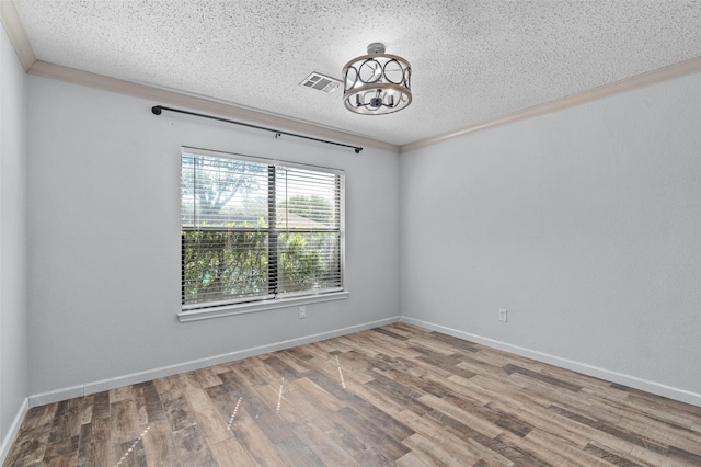 spare room with wood finished floors, visible vents, ornamental molding, a textured ceiling, and a notable chandelier