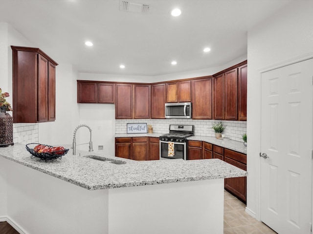 kitchen with visible vents, a sink, appliances with stainless steel finishes, a peninsula, and light stone counters