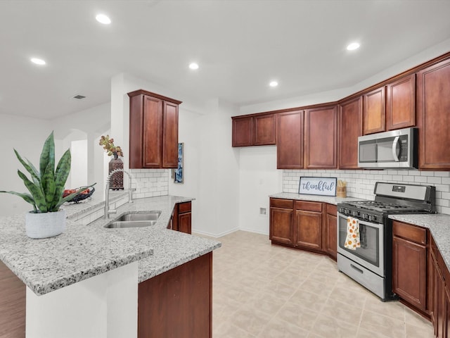 kitchen with recessed lighting, a peninsula, light stone countertops, appliances with stainless steel finishes, and a sink