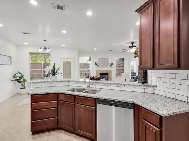 kitchen with ceiling fan with notable chandelier, stainless steel dishwasher, a fireplace, light stone countertops, and a sink