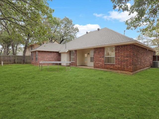 back of property featuring roof with shingles, brick siding, a yard, and fence