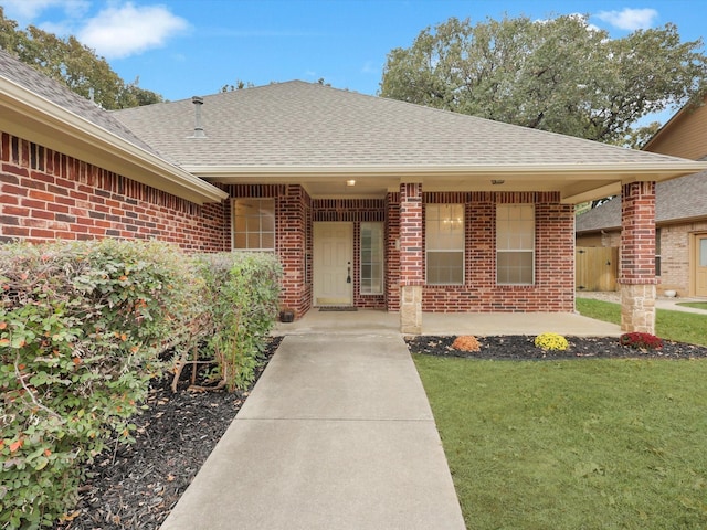 doorway to property with a lawn, brick siding, and a shingled roof