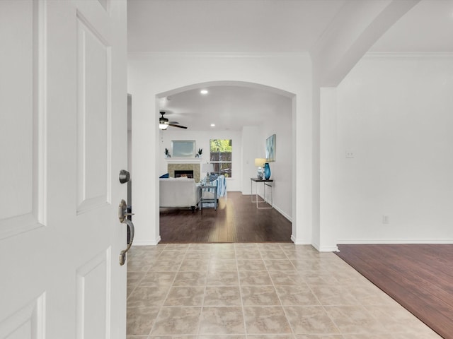 tiled foyer entrance featuring ornamental molding, ceiling fan, arched walkways, and a fireplace
