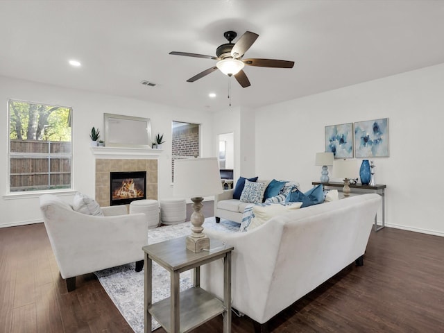 living area featuring a fireplace, a ceiling fan, visible vents, dark wood-style flooring, and baseboards