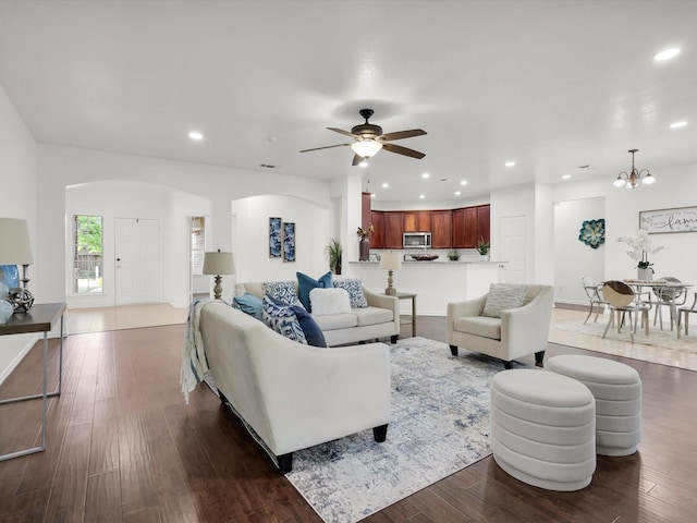 living area with dark wood-style flooring, recessed lighting, arched walkways, and ceiling fan with notable chandelier
