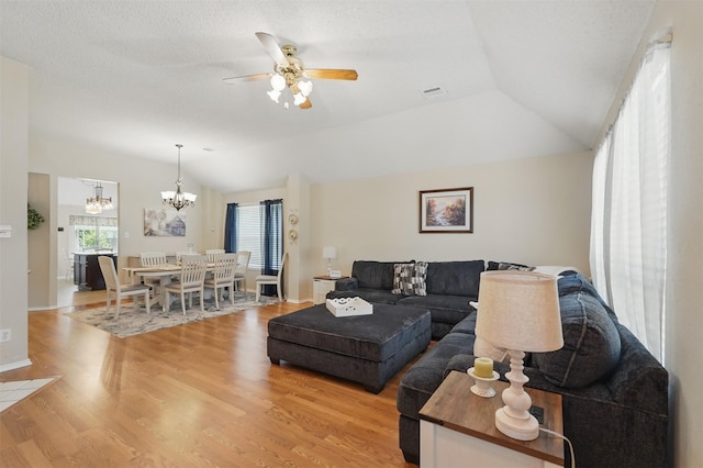 living area featuring light wood finished floors, visible vents, ceiling fan with notable chandelier, and vaulted ceiling