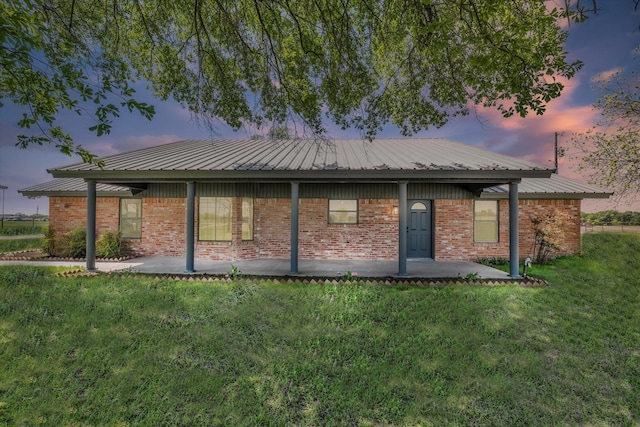 back of property featuring brick siding, a patio area, metal roof, and a lawn
