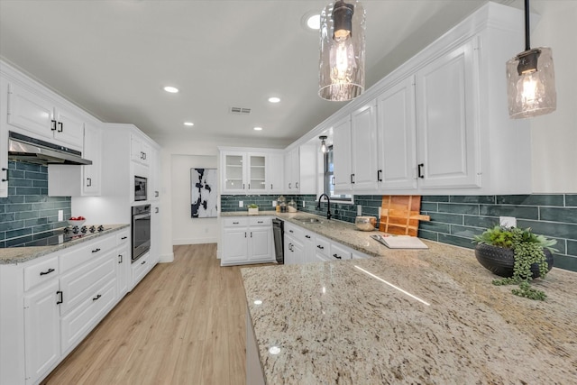 kitchen featuring white cabinets, under cabinet range hood, black appliances, decorative backsplash, and a sink