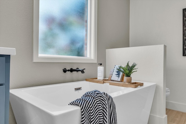 bathroom featuring a freestanding tub, toilet, and wood finished floors