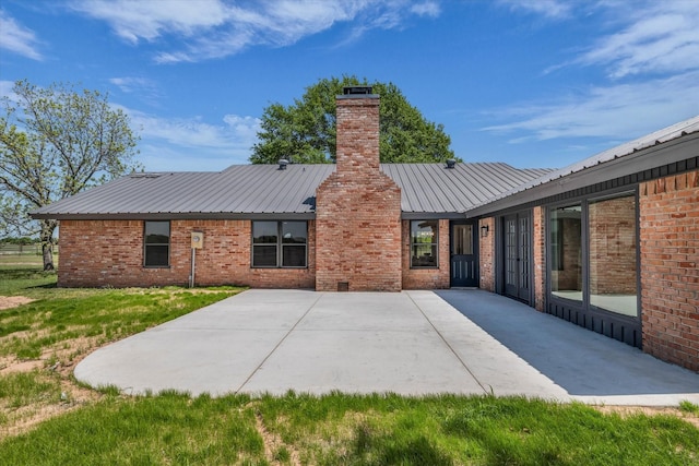 back of property with a patio, a chimney, metal roof, and brick siding