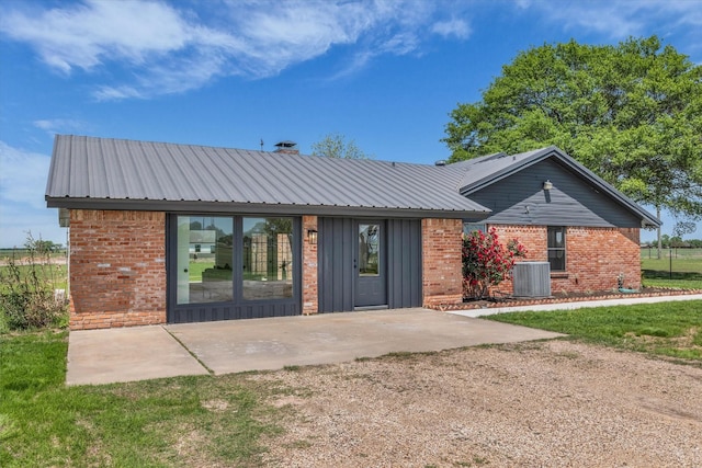 rear view of property with central air condition unit, metal roof, and brick siding