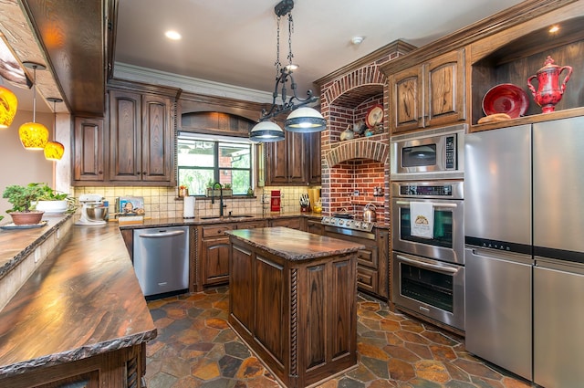 kitchen featuring tasteful backsplash, stone finish flooring, stainless steel appliances, a sink, and hanging light fixtures