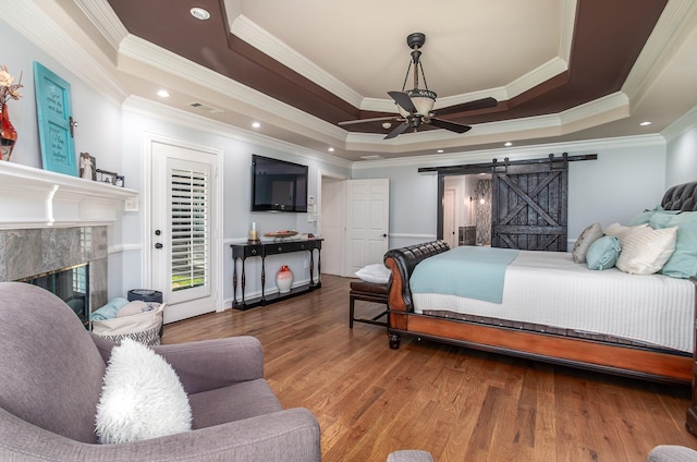 bedroom featuring ornamental molding, a tray ceiling, a barn door, and wood finished floors