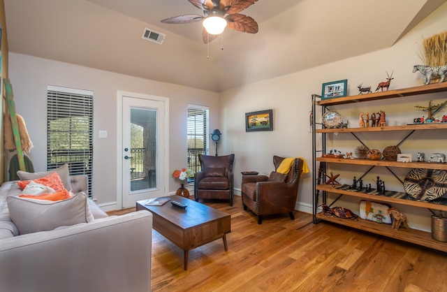 living area featuring light wood-type flooring, a ceiling fan, vaulted ceiling, visible vents, and baseboards