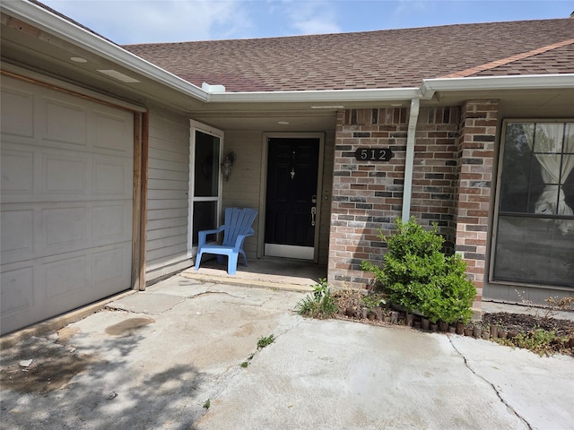 entrance to property featuring a shingled roof, brick siding, and an attached garage