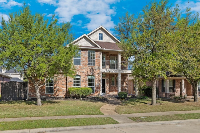 view of front of property with brick siding, a front lawn, fence, and a balcony