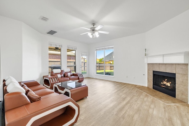 living room featuring wood finished floors, ceiling fan, a tiled fireplace, and visible vents