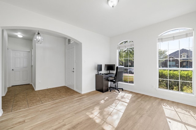 office area with baseboards, light wood finished floors, and arched walkways