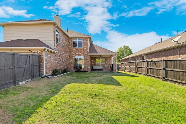 back of house featuring a chimney, a fenced backyard, a ceiling fan, and a lawn