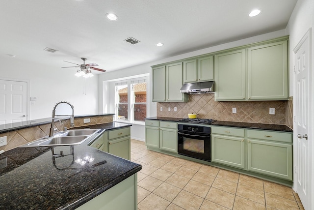 kitchen with green cabinets, under cabinet range hood, a sink, black oven, and decorative backsplash