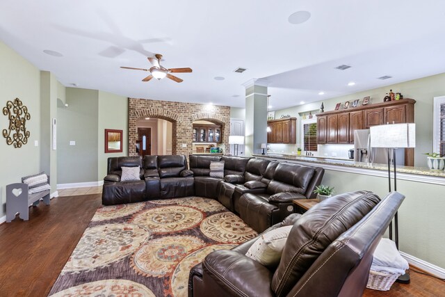 living room featuring dark wood finished floors, arched walkways, ceiling fan, baseboards, and ornate columns