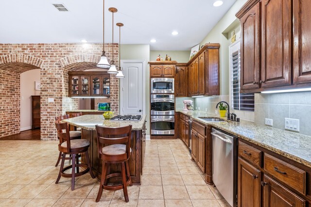 kitchen featuring a sink, appliances with stainless steel finishes, light tile patterned floors, a kitchen breakfast bar, and brick wall