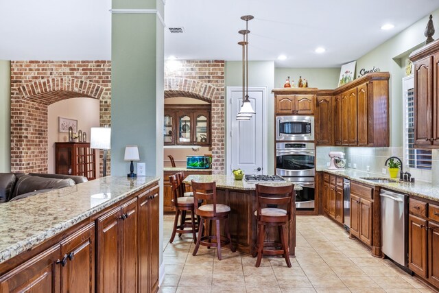 kitchen with stainless steel appliances, a sink, a kitchen bar, light stone counters, and brick wall