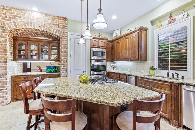 kitchen featuring stainless steel appliances, a sink, a kitchen bar, a center island, and light stone counters